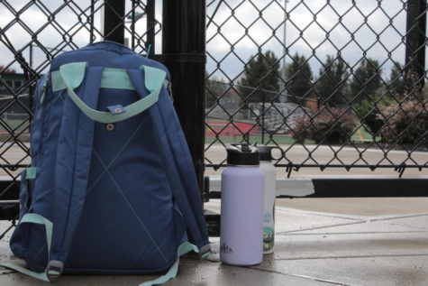 A backpack and water bottles sit outside the fences surrounding the football field. 